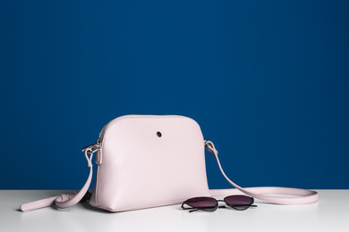 Photo of Stylish woman's bag and sunglasses on white table. Space for text