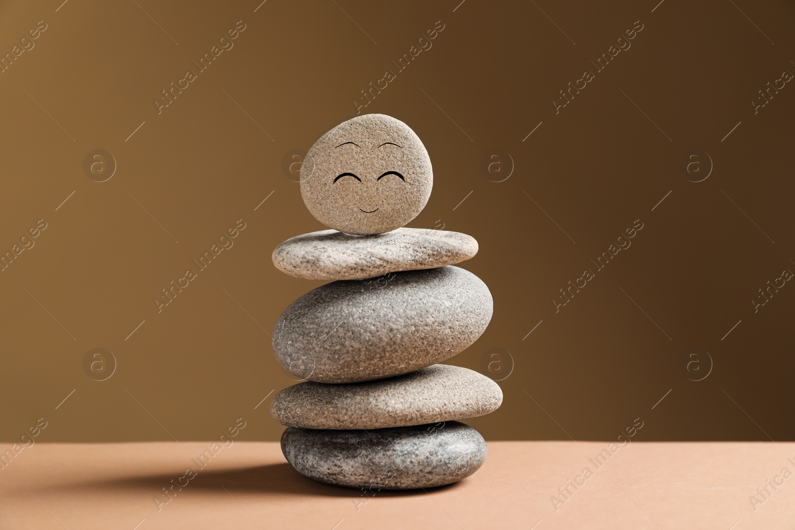 Photo of Stack of stones with drawn happy face on table against dark beige background. Zen concept