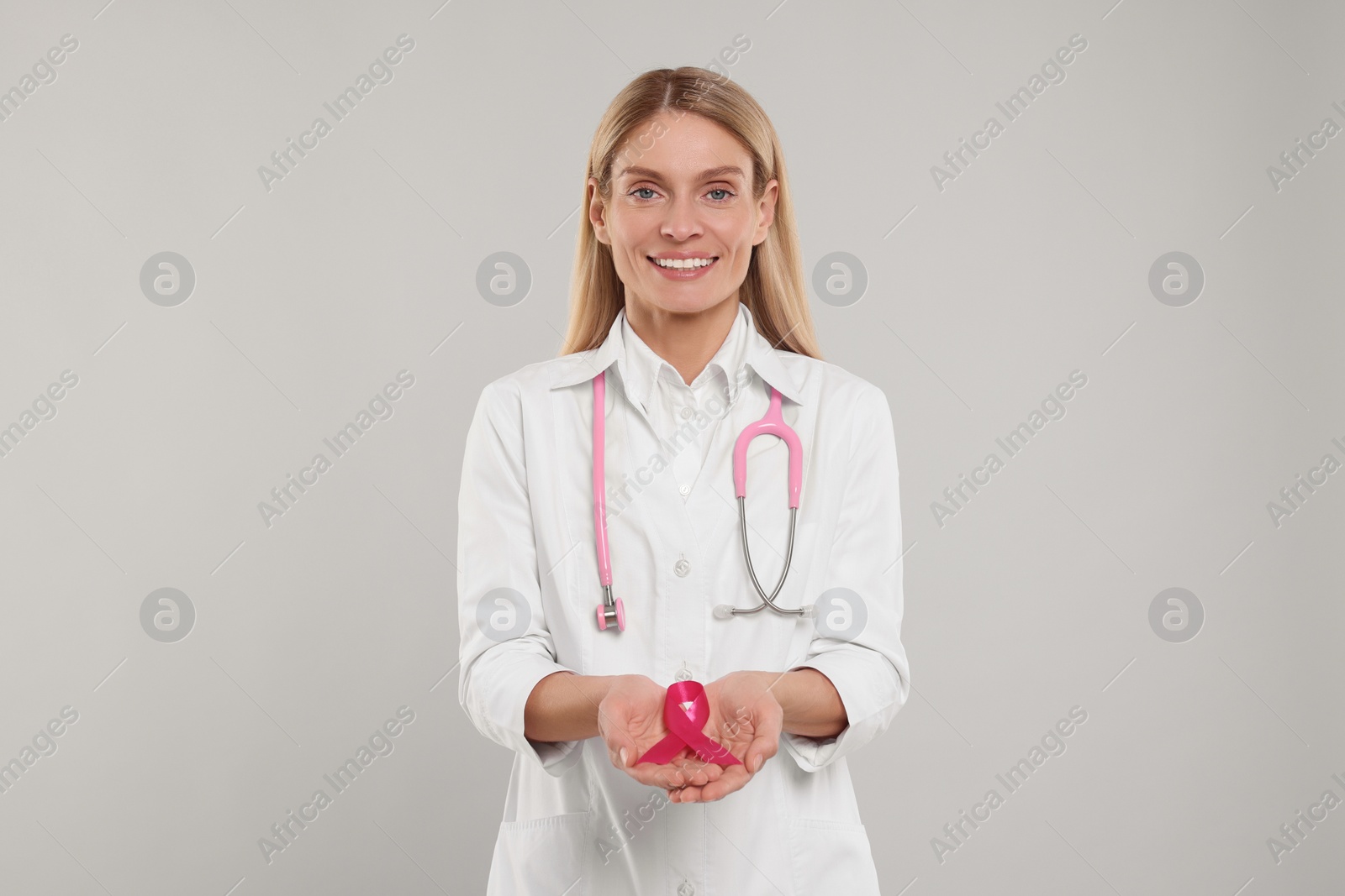 Photo of Doctor with stethoscope holding pink ribbon on light grey background. Breast cancer awareness