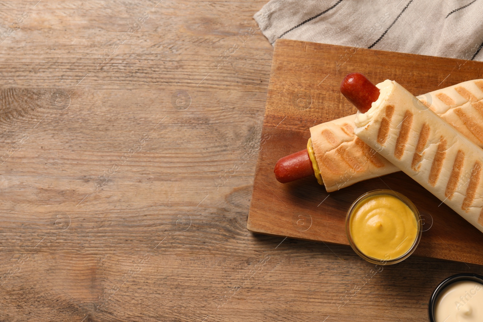 Photo of Tasty french hot dogs with different sauces on wooden table, flat lay. Space for text