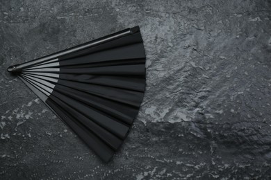 Stylish black hand fan on grey textured background, top view. Space for text