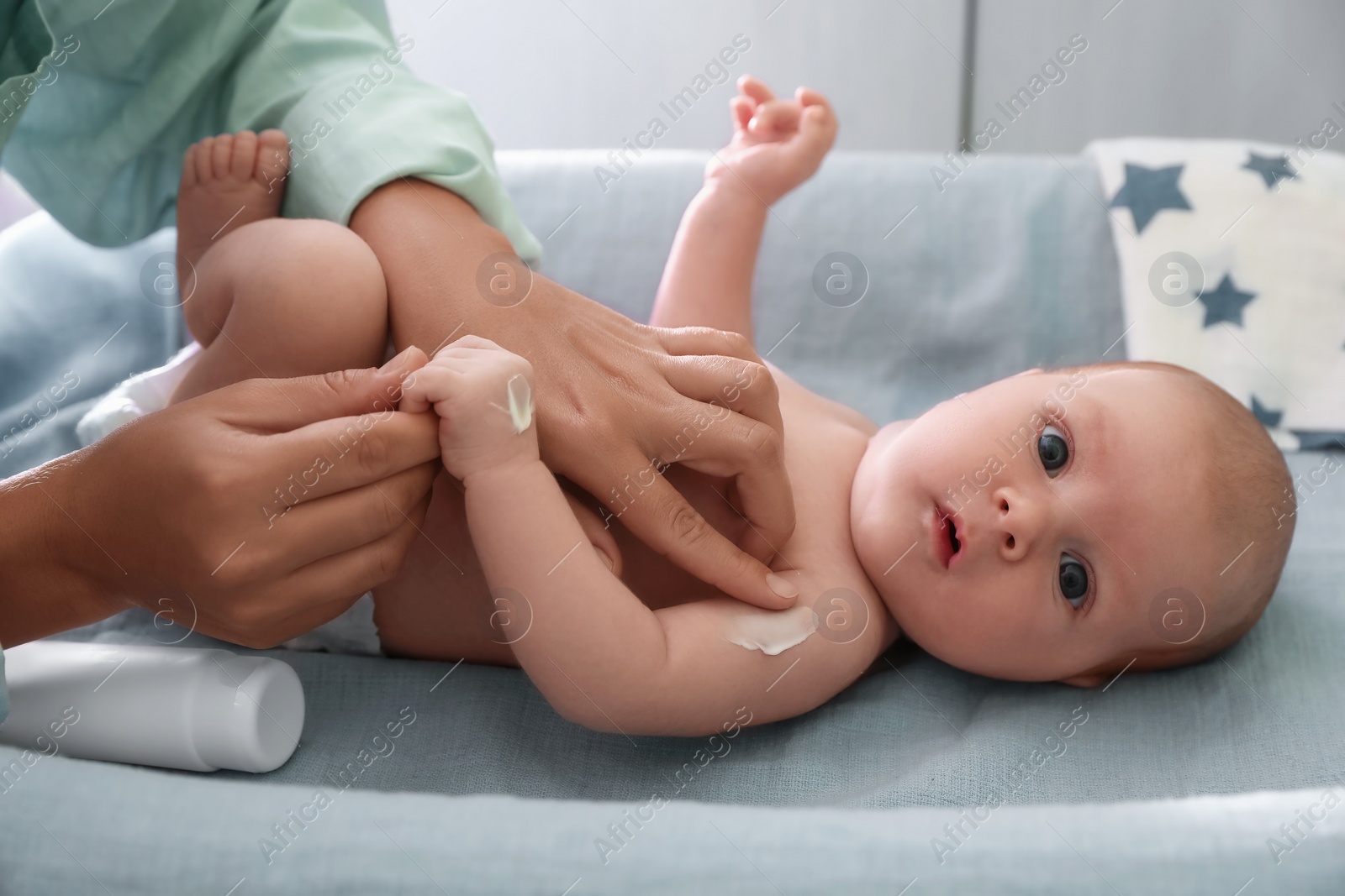 Photo of Mother applying moisturizing cream onto baby`s arm on changing table indoors, closeup