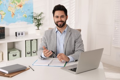Happy manager with notebook sitting at desk in travel agency