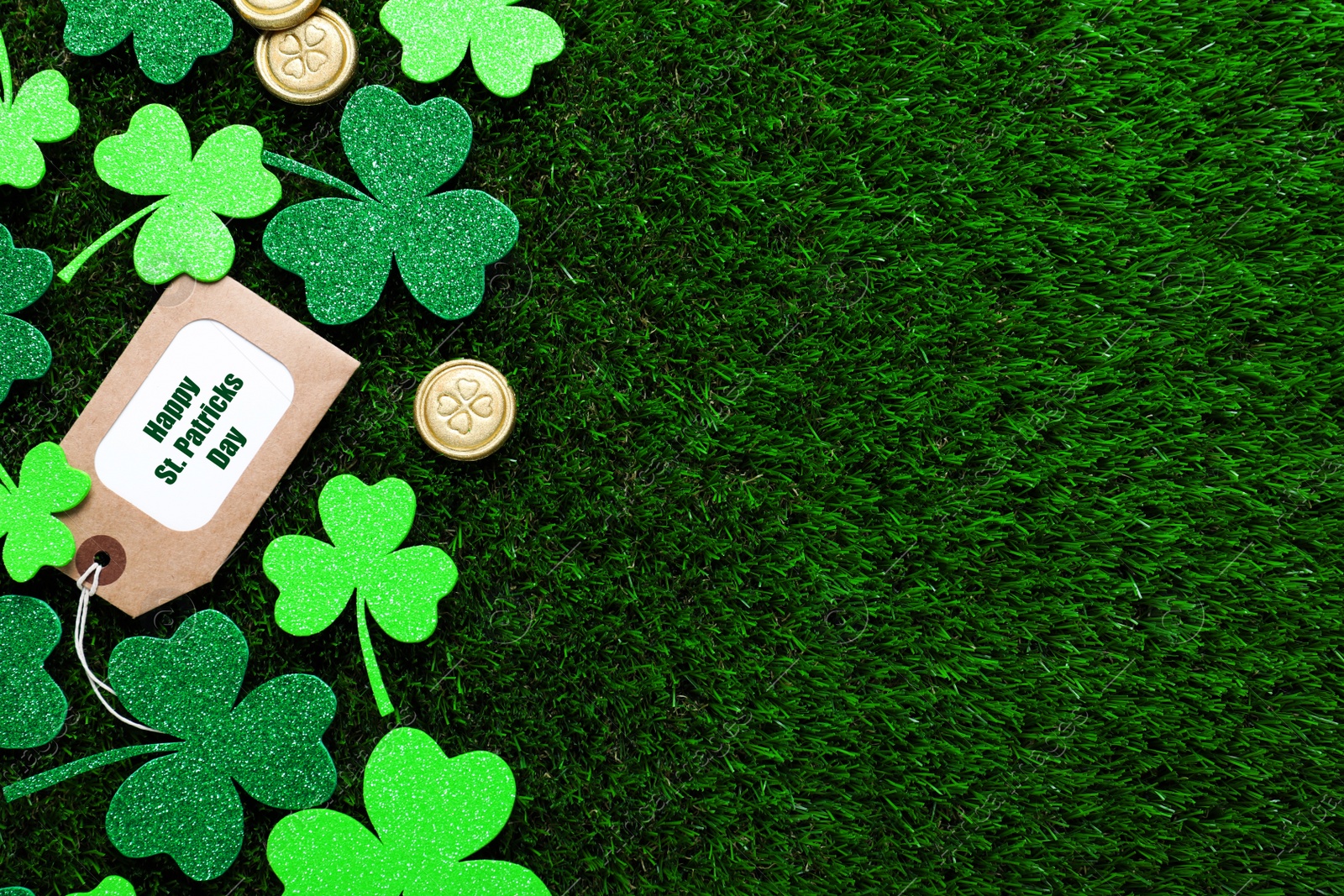 Photo of Flat lay composition with clover leaves and gold coins on green grass, space for text. St. Patrick's Day celebration