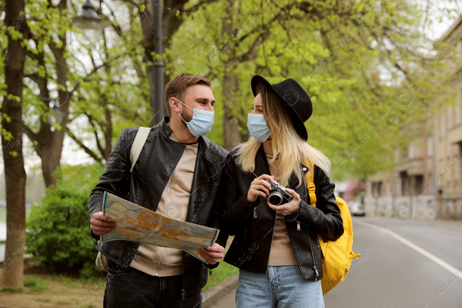 Photo of Couple of tourists in medical masks with map and camera on city street