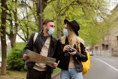 Couple of tourists in medical masks with map and camera on city street