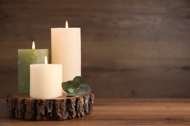 Photo of Beautiful candles and eucalyptus branch on wooden table, space for text