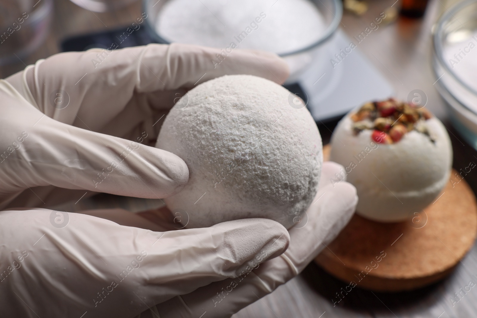 Photo of Woman holding handmade bath bomb above wooden table, closeup