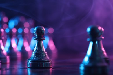 Chess pawns on checkerboard in color light, selective focus. Space for text