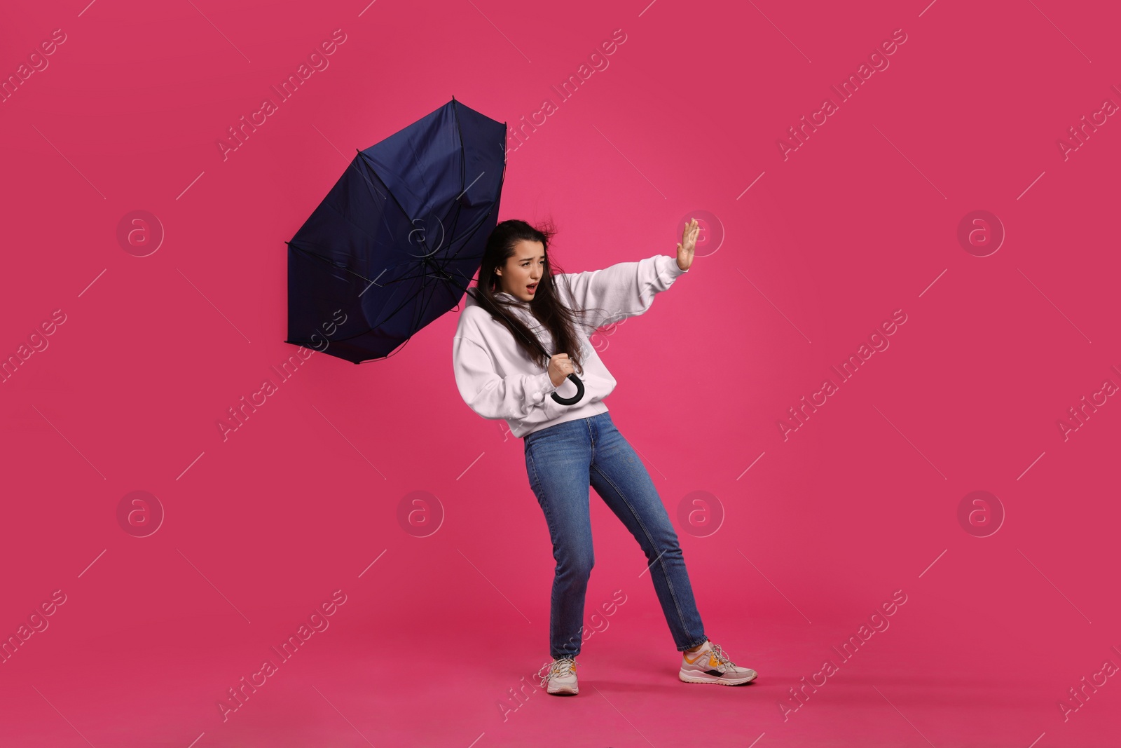 Photo of Emotional woman with umbrella caught in gust of wind on pink background