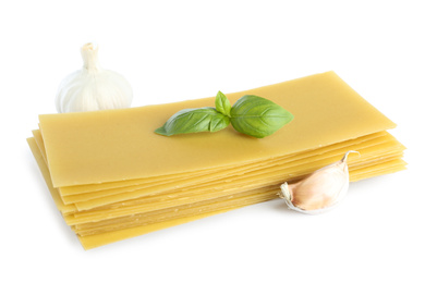Photo of Uncooked lasagna sheets, garlic and basil on white background