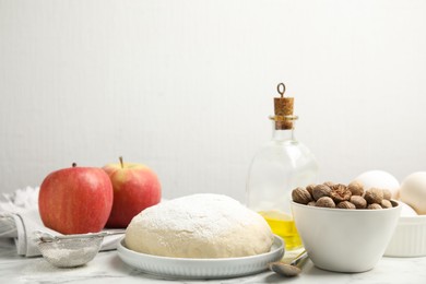 Photo of Raw dough, nutmeg seeds and other ingredients for pastry on marble table against white background