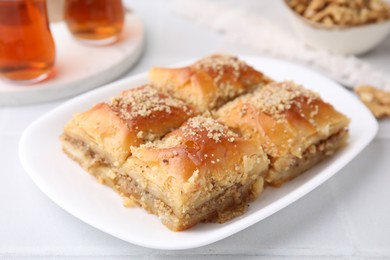 Photo of Eastern sweets. Pieces of tasty baklava and tea on white tiled table, closeup