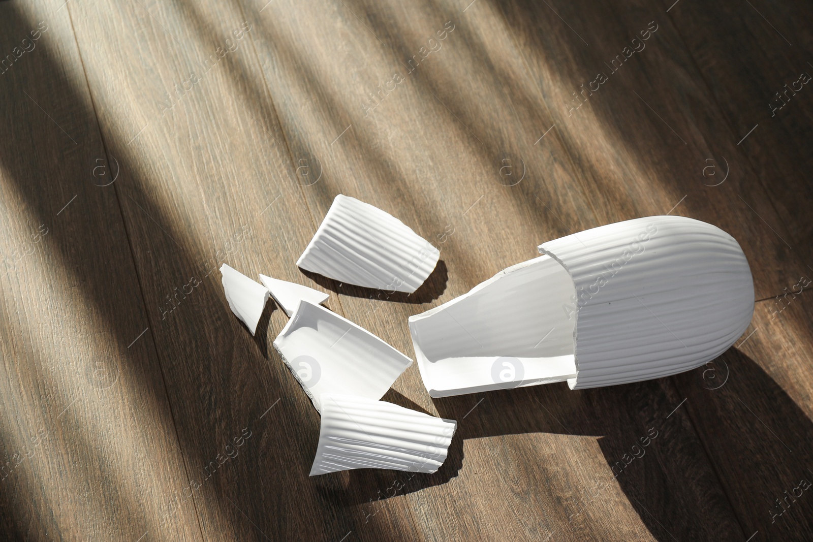 Photo of Broken white ceramic vase on wooden floor, above view