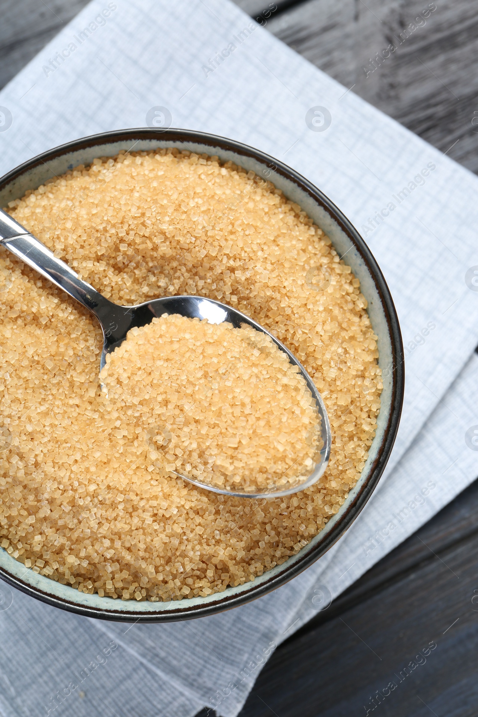 Photo of Brown sugar in bowl and spoon on black wooden table, top view