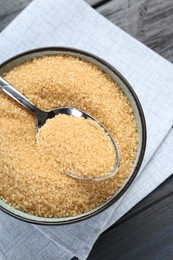 Photo of Brown sugar in bowl and spoon on black wooden table, top view