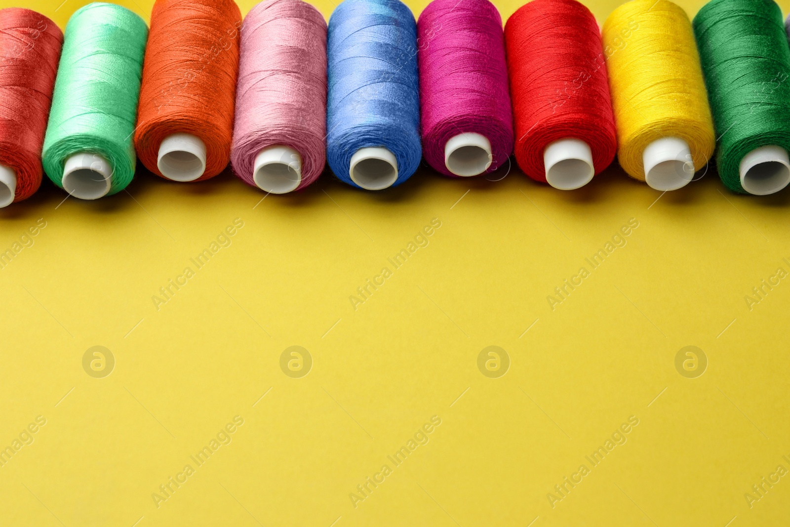 Photo of Set of colorful sewing threads on yellow background. Space for text