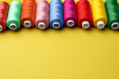 Photo of Set of colorful sewing threads on yellow background. Space for text