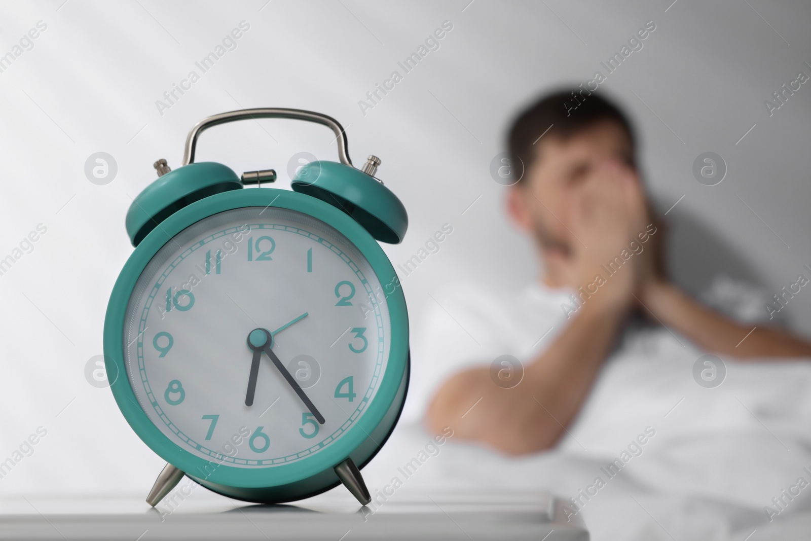 Photo of Sleepy man awaking at home in morning, focus on alarm clock. Space for text