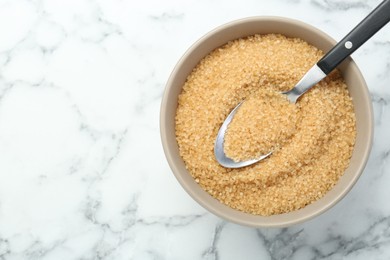 Brown sugar in bowl and spoon on white marble table, top view. Space for text