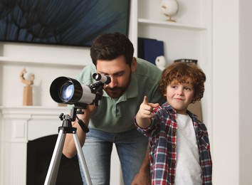 Little boy with his father looking at stars through telescope in room