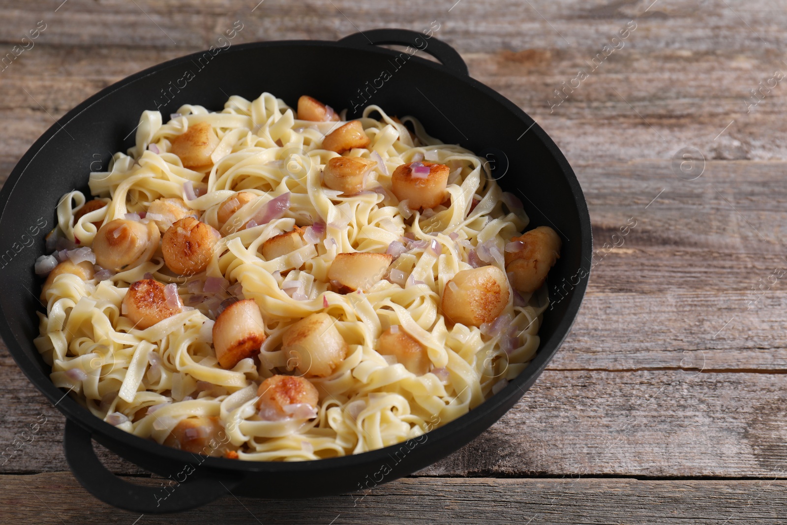 Photo of Delicious scallop pasta with onion in pan on wooden table, closeup