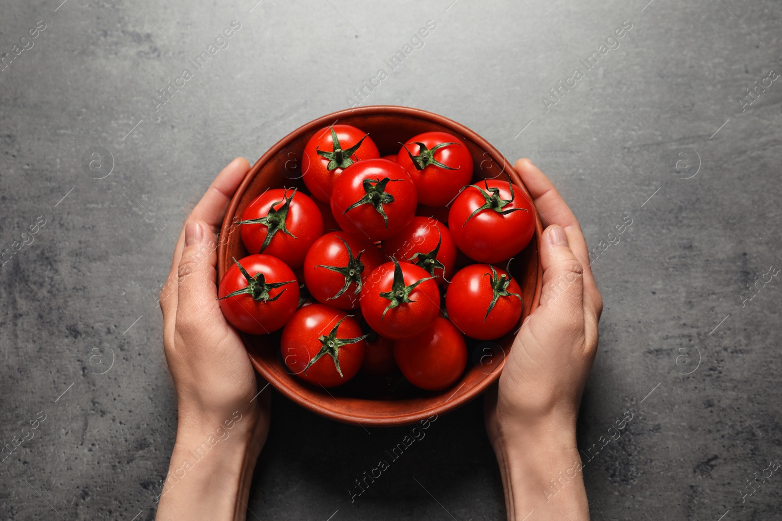 Photo of Woman holding wooden bowl with ripe cherry tomatoes at table, above view