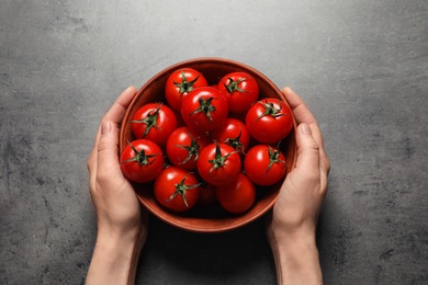 Woman holding wooden bowl with ripe cherry tomatoes at table, above view