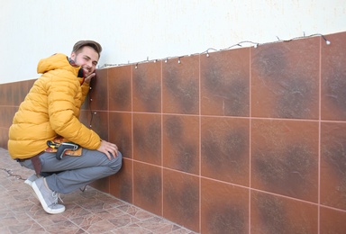 Photo of Young man decorating outdoor wall with Christmas lights