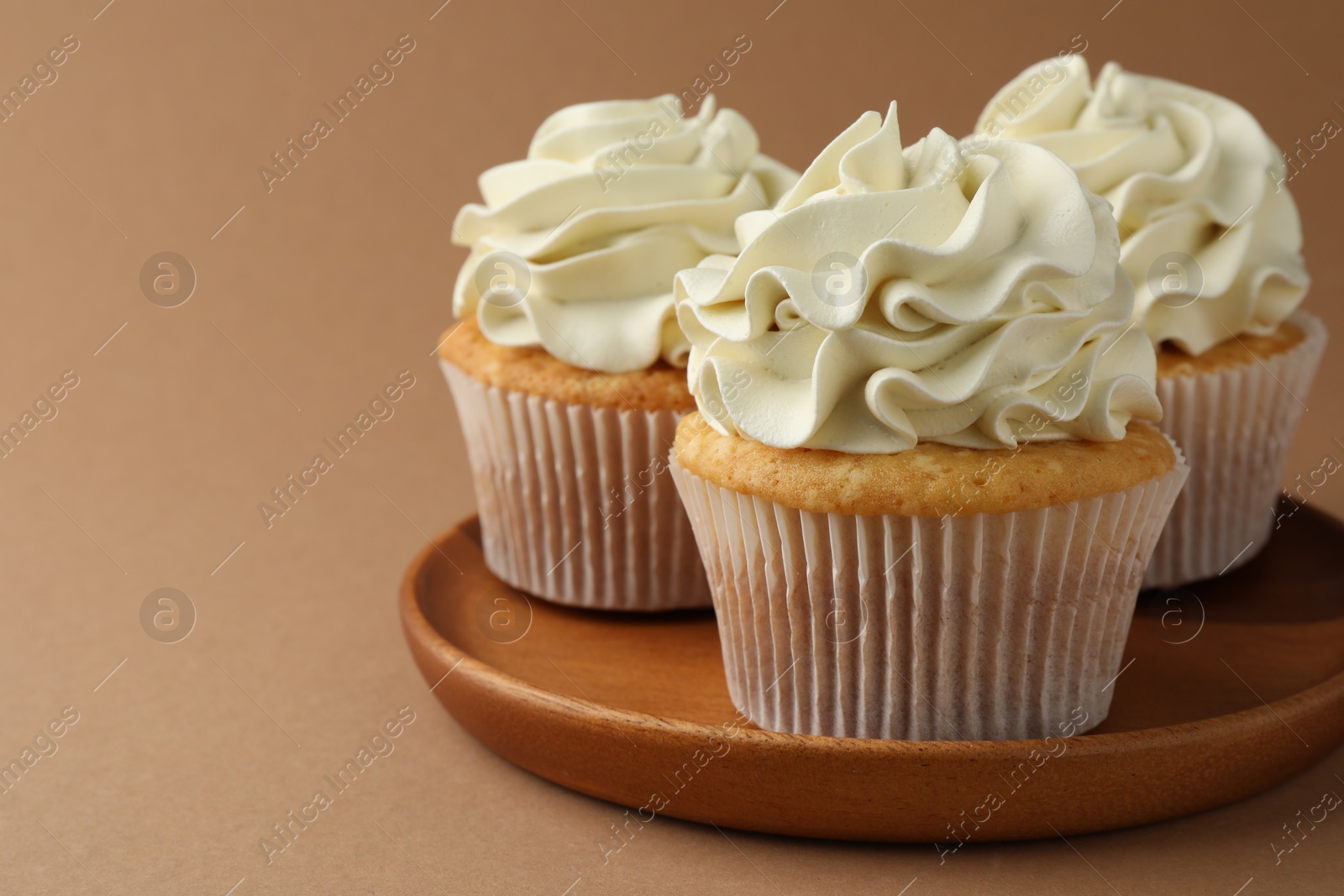 Photo of Tasty vanilla cupcakes with cream on dark beige background, closeup. Space for text