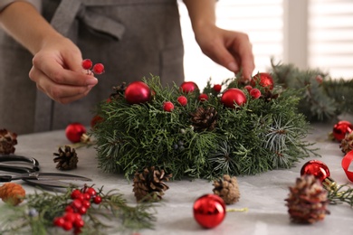 Florist making beautiful Christmas wreath at grey table indoors, closeup