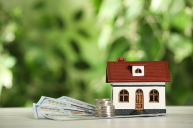 Photo of Mortgage concept. House model and money on white table against blurred background, space for text