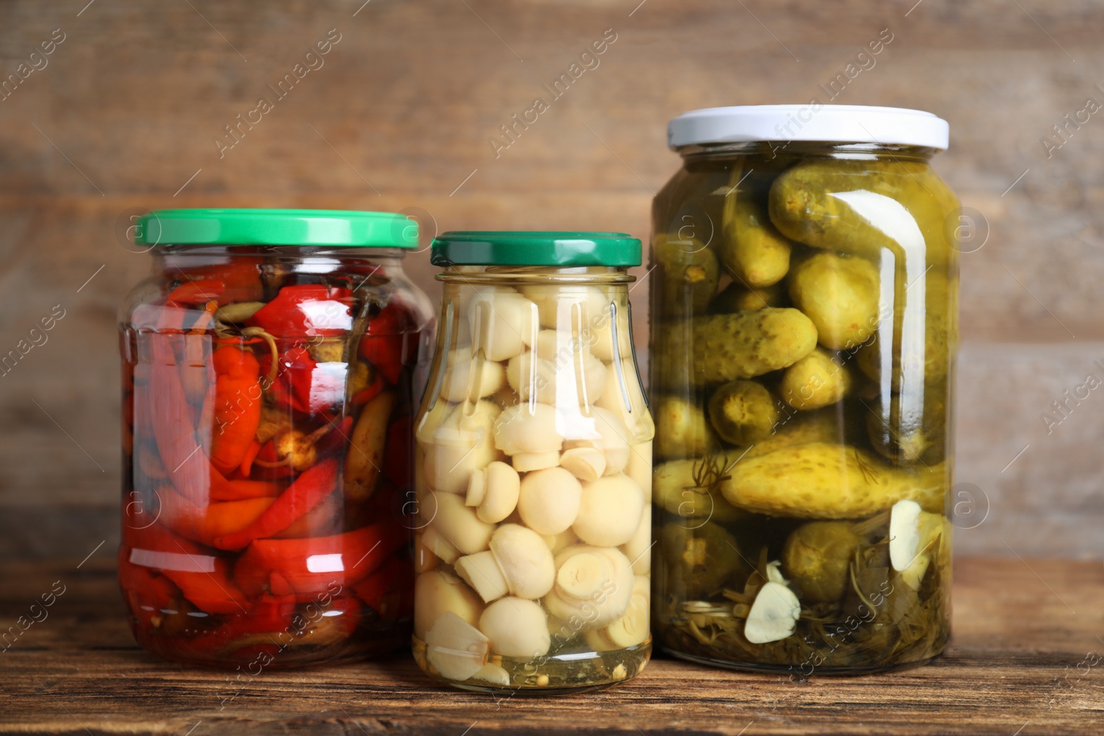 Photo of Glass jars with different pickled vegetables on wooden table