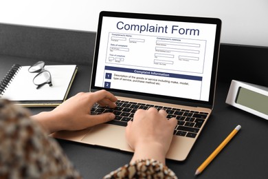 Woman filling online complaint form via laptop at table, closeup