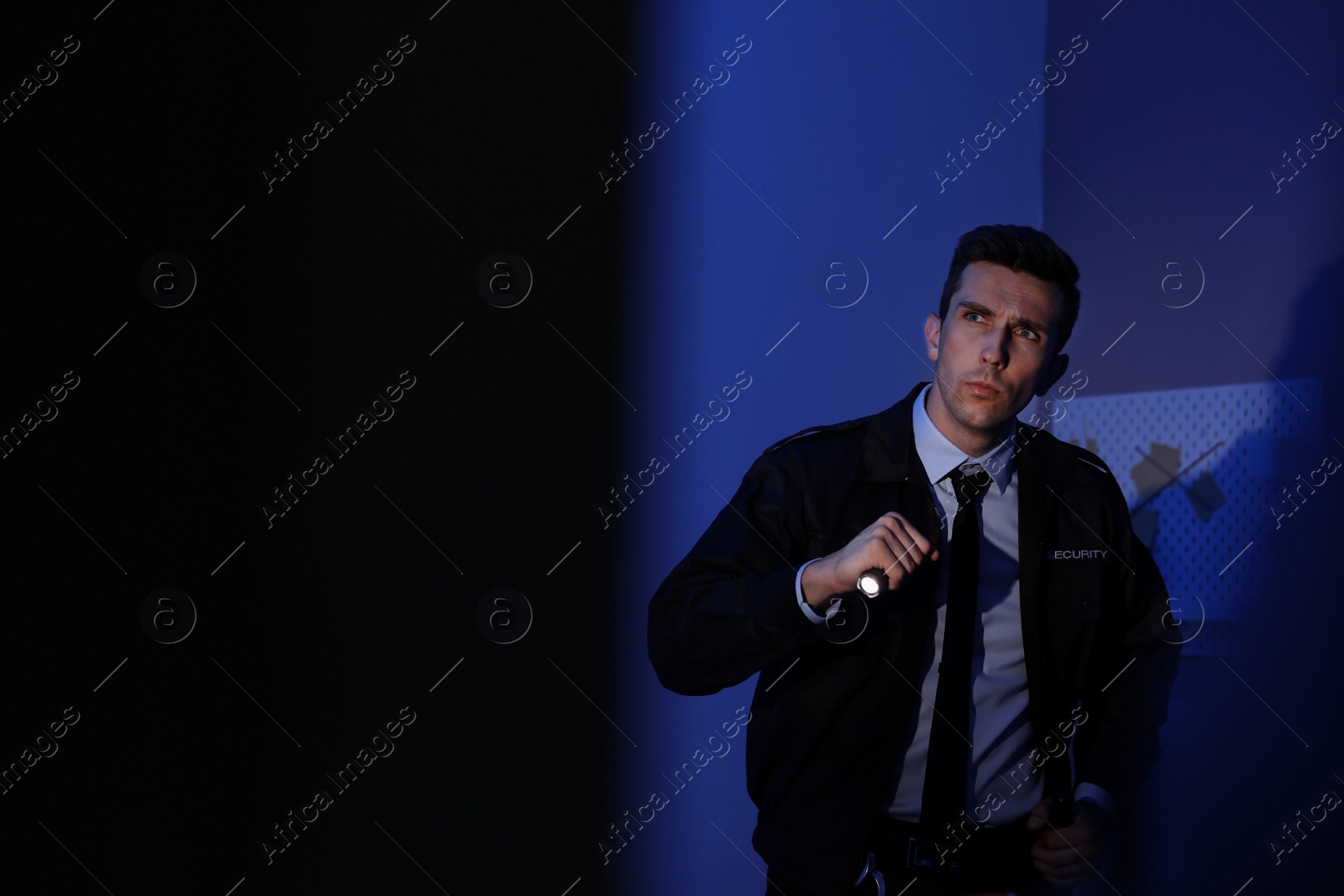 Photo of Male security guard with flashlight in dark room