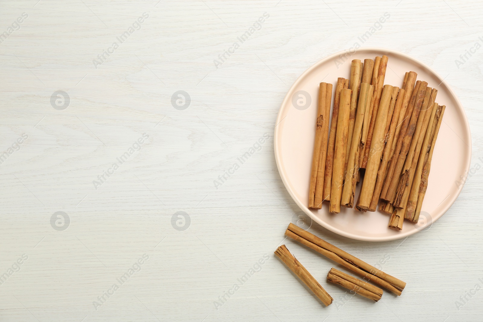 Photo of Aromatic cinnamon sticks on white wooden table, flat lay. Space for text