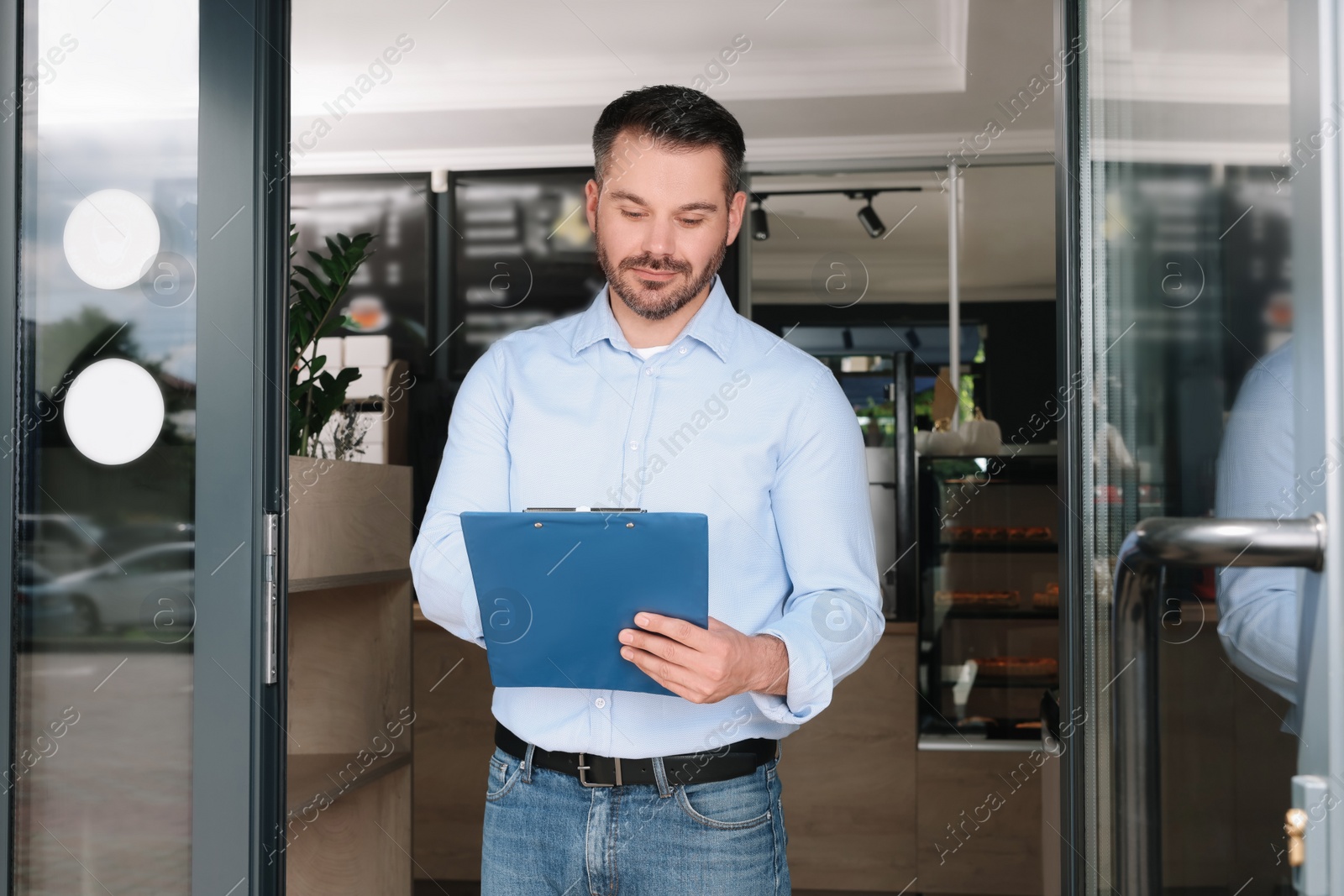 Photo of Business owner with clipboard at door of his cafe