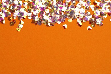 Photo of Pile of shiny glitter on orange background, flat lay. Space for text