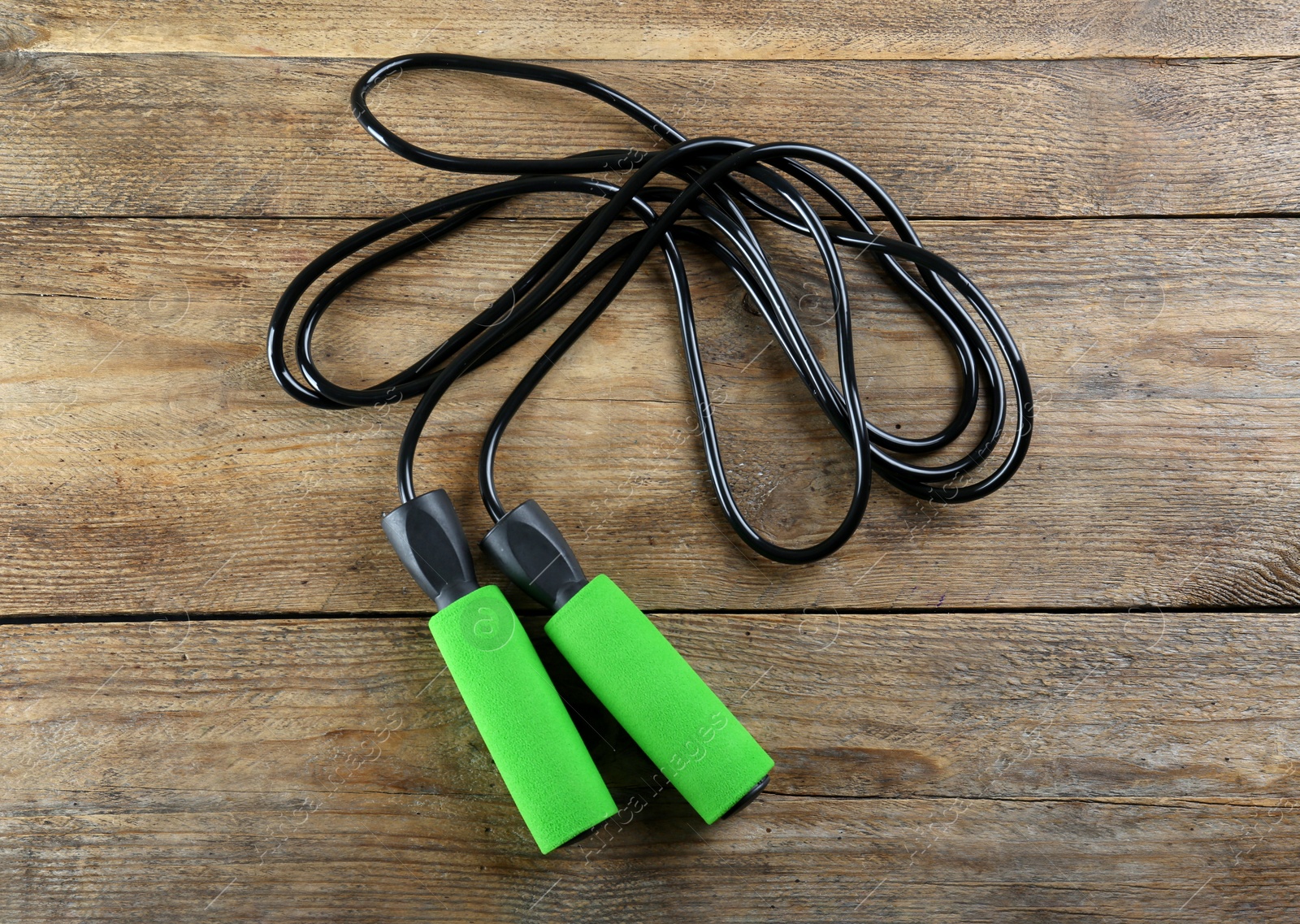 Photo of Skipping rope on wooden table, top view. Sports equipment