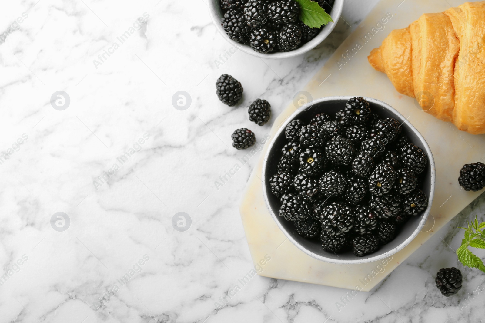 Photo of Bowl of fresh ripe blackberries on white marble table, flat lay. Space for text