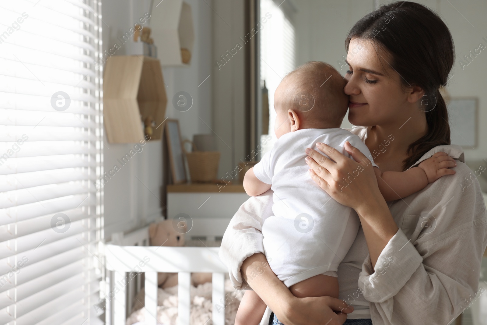 Photo of Happy young mother with her baby near window at home. Space for text