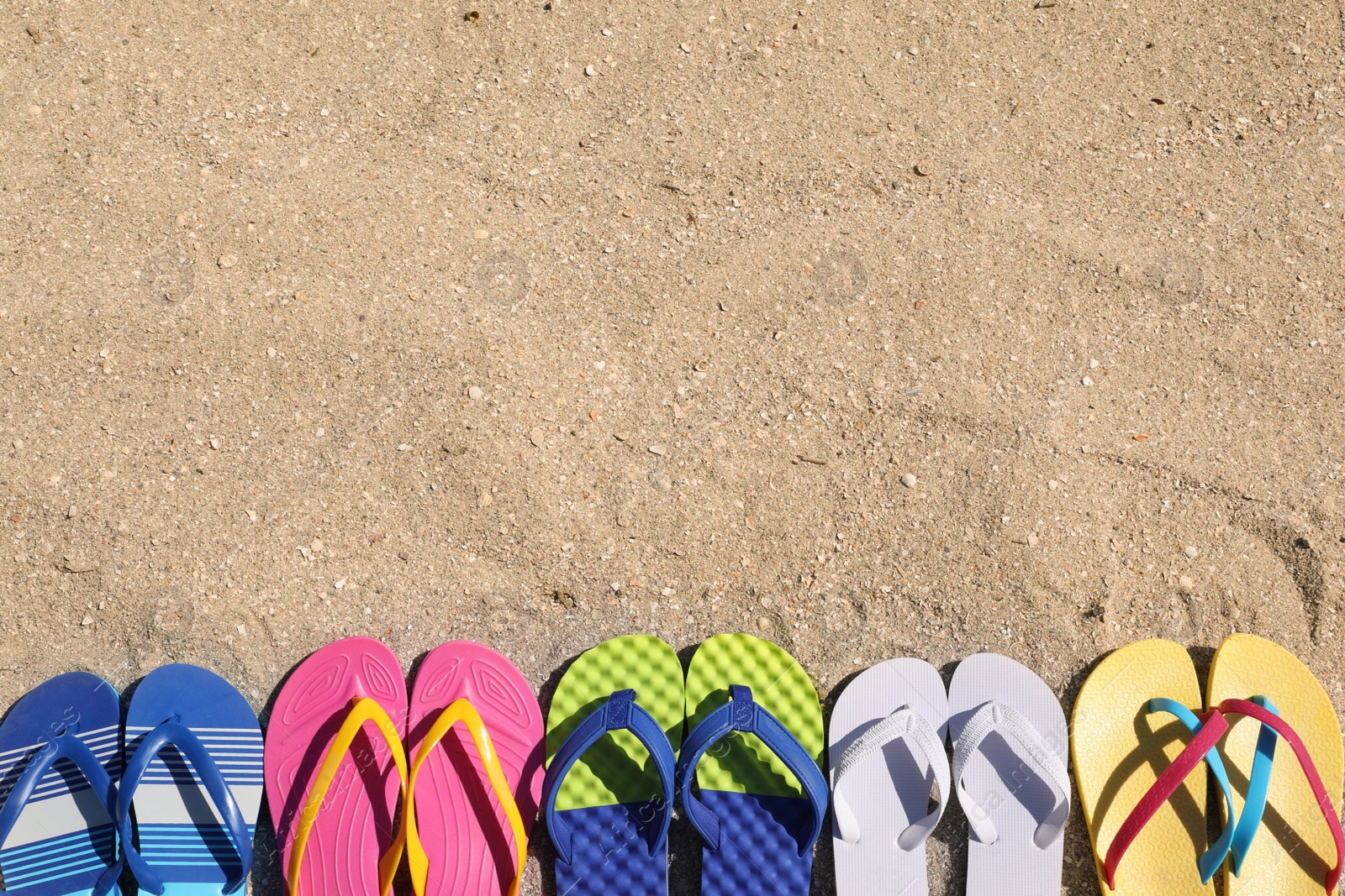 Photo of Many different flip flops on sand, flat lay. Space for text