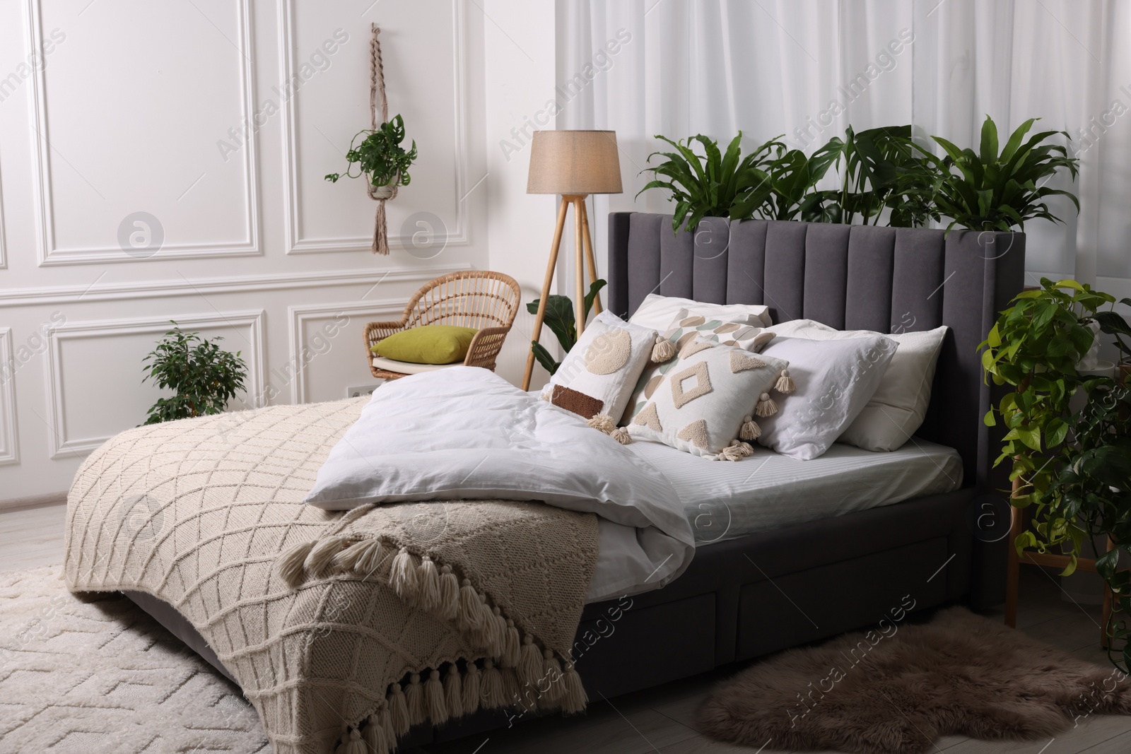 Photo of Large comfortable bed, lamp and beautiful houseplants in bedroom. Interior design