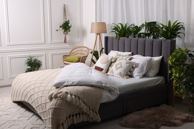 Large comfortable bed, lamp and beautiful houseplants in bedroom. Interior design