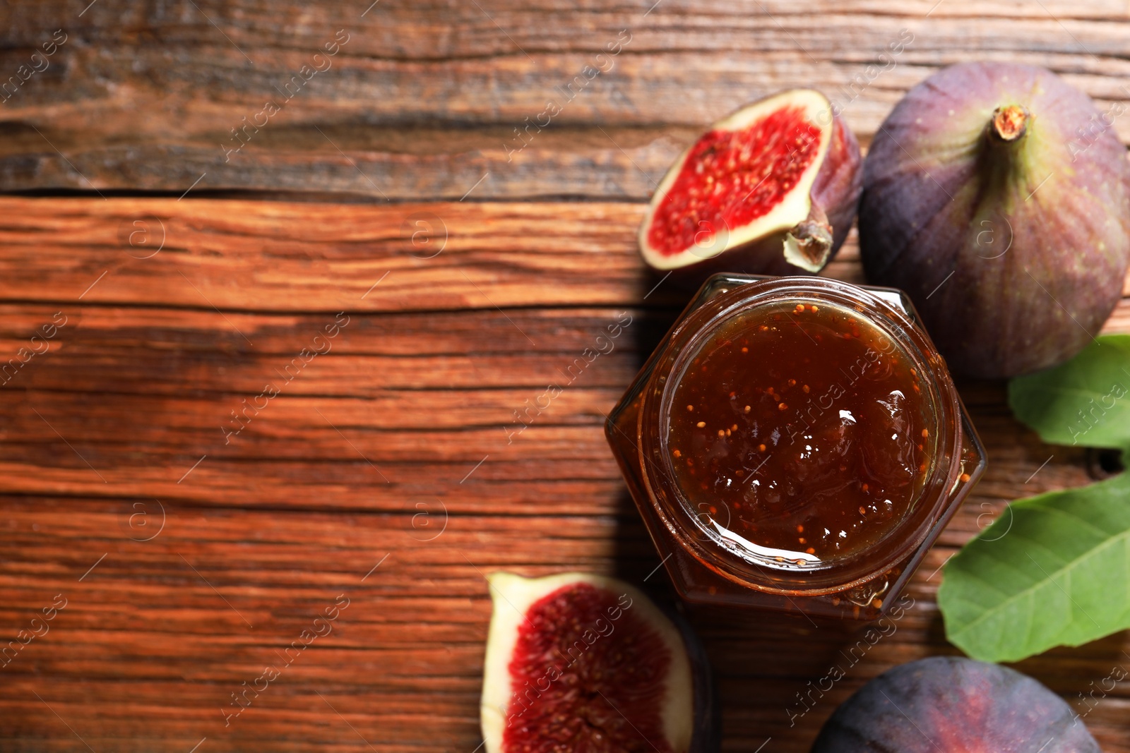 Photo of Jar of tasty sweet jam and fresh figs on wooden table, flat lay. Space for text