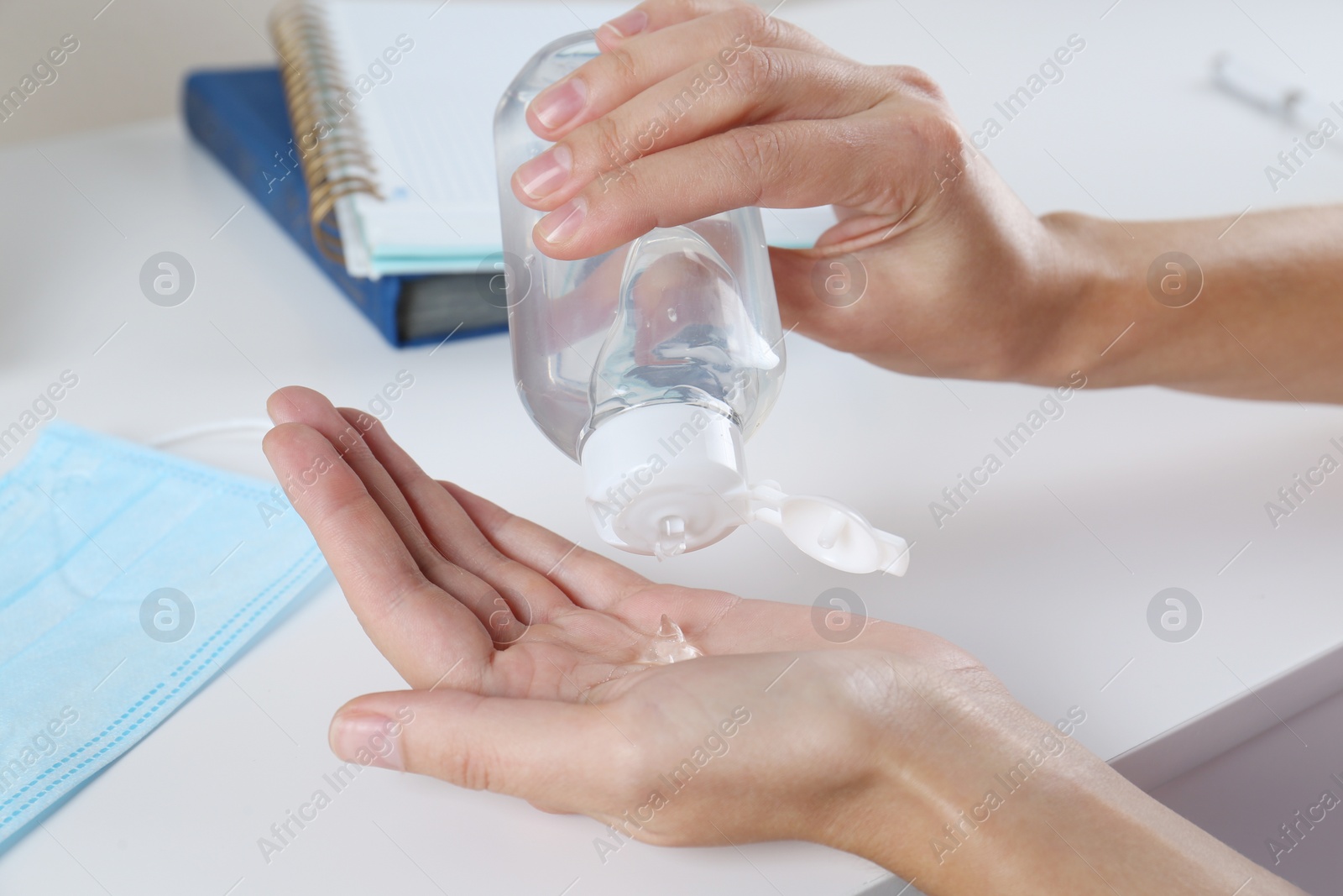 Photo of Woman applying hand sanitizer at white table in office, closeup. Personal hygiene during COVID-19 pandemic