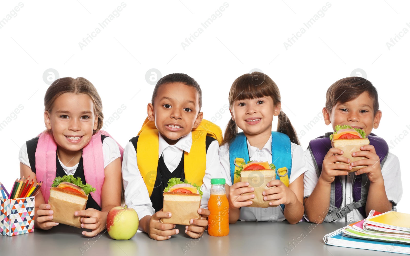 Photo of Schoolchildren with healthy food and backpacks sitting at table on white background