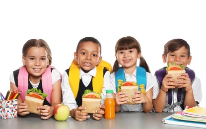 Schoolchildren with healthy food and backpacks sitting at table on white background