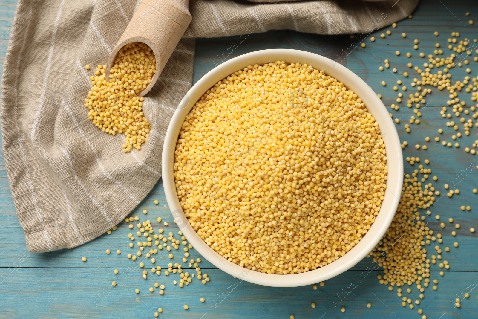 Photo of Millet groats in bowl and scoop on light blue wooden table, flat lay