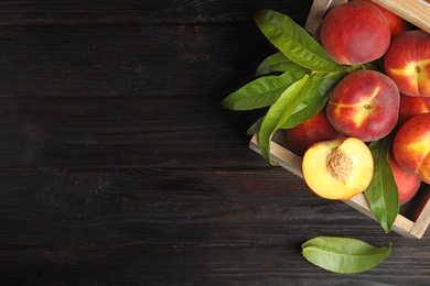 Photo of Wooden crate with tasty peaches on black table, top view. Space for text